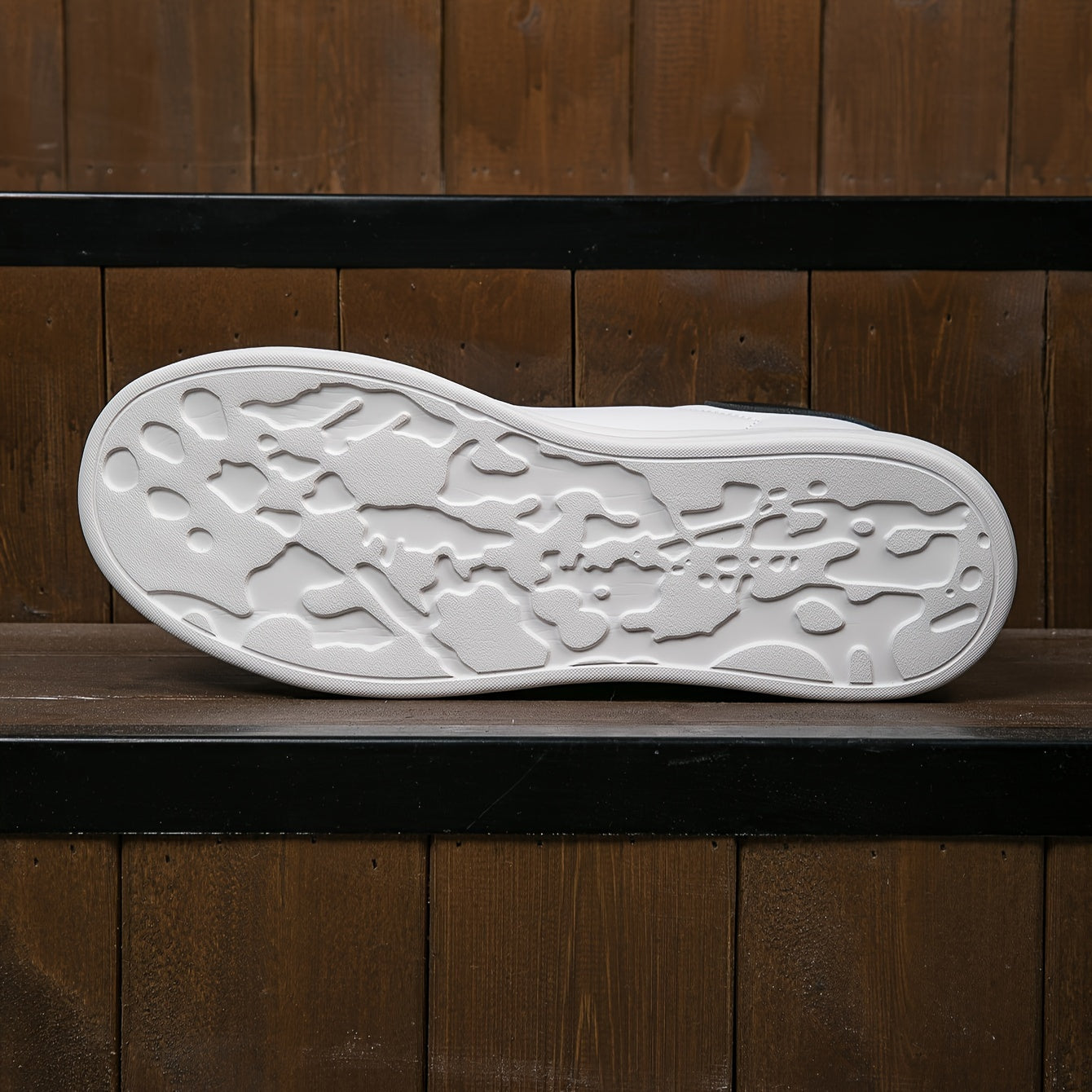 Hvid sneakersål med unikt mønster på træbaggrund. Moderne skodesign, komfortabelt fodtøj, stilfuld sneaker til hverdagsbrug.