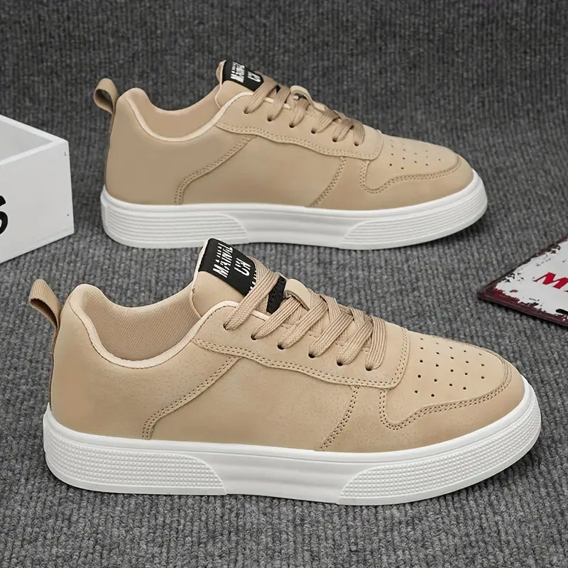 Beige sneakers med hvid sål på gråt tæppe. Moderne herresko, snørebånd, perforeret design. Stilfuldt fodtøj til hverdagsbrug.