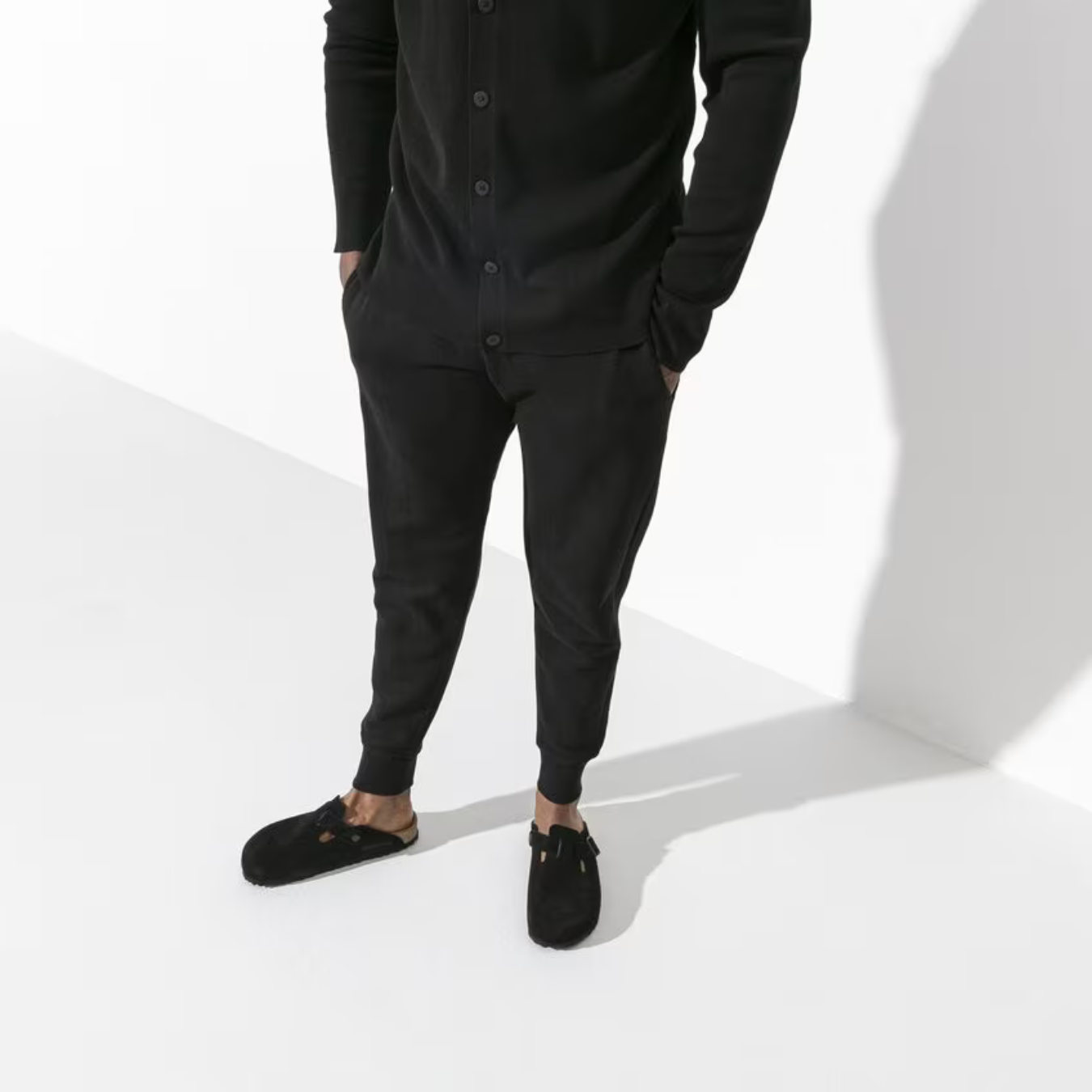 Mand iført sort cardigan, joggers og sorte Birkenstock Boston hjemmesko. Minimalistisk herremode, komfortabelt tøj, moderne stil.