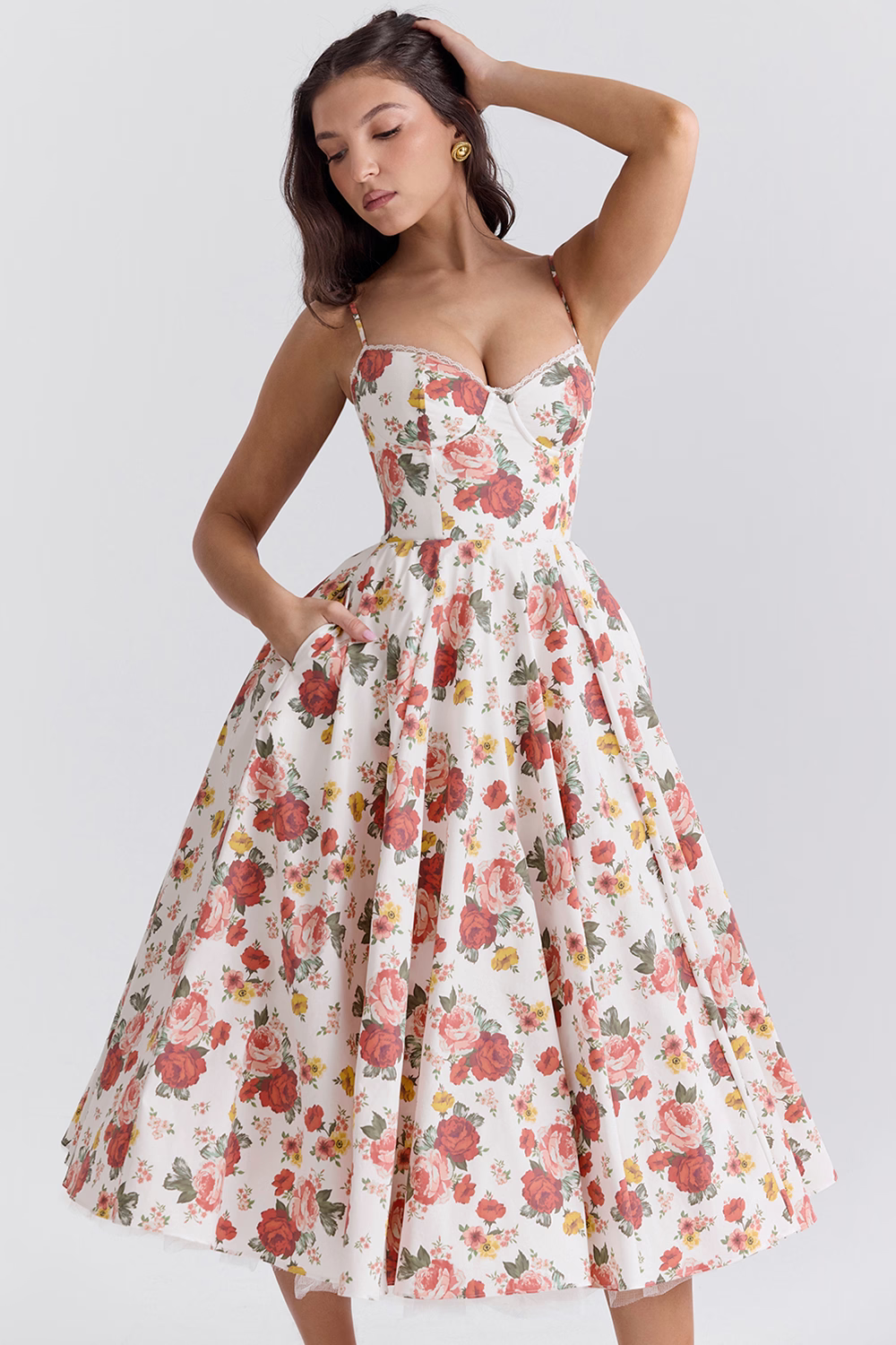 Ung kvinde i en blomsterprintet sommerkjole med lommer, poserer elegant. Kjolen har en vintage stil med et feminint snit, perfekt til sommermode.