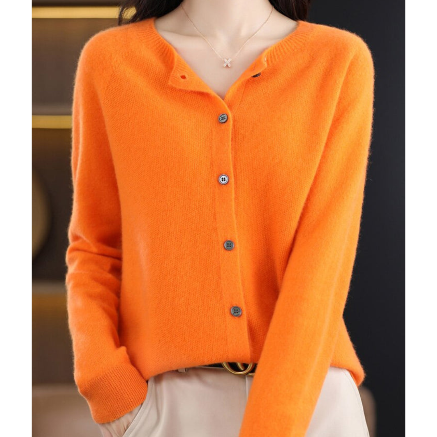 Kvinde iført orange cardigan med knapper, beige bukser. Stilfuldt efterårsoutfit, blødt strik, trendy mode. Perfekt til kølige dage.
