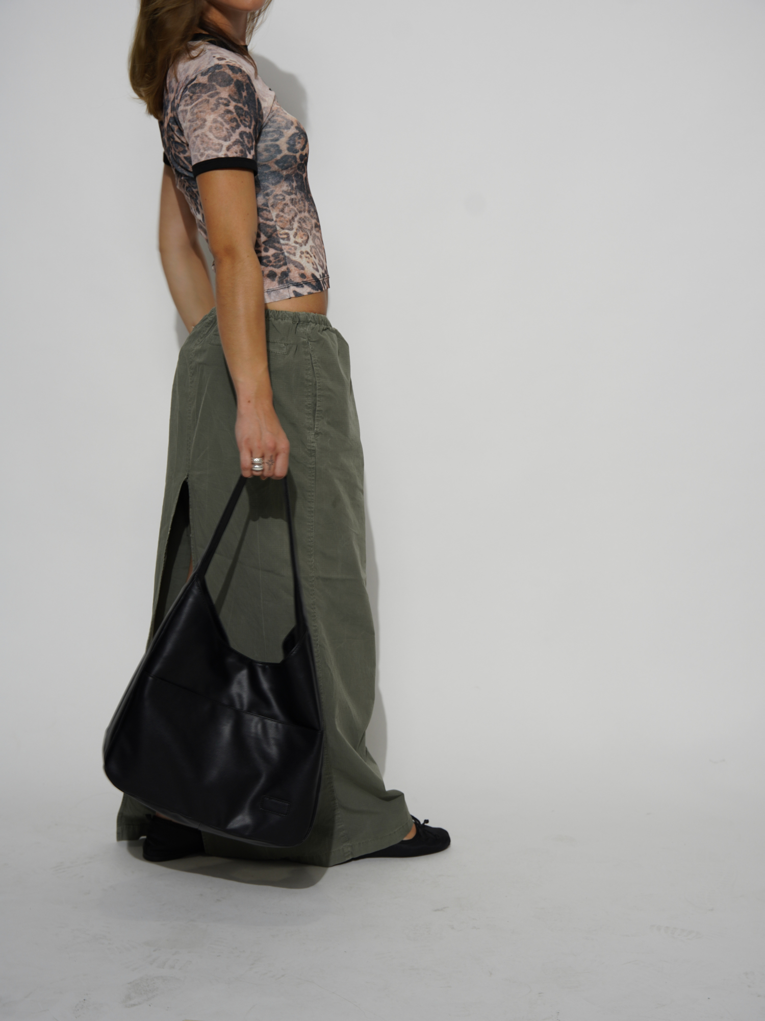 Kvinde i leopardmønstret top og grønne bukser, bærer sort lædertaske. Mode, stilfuldt outfit, moderne tøj, casual look.