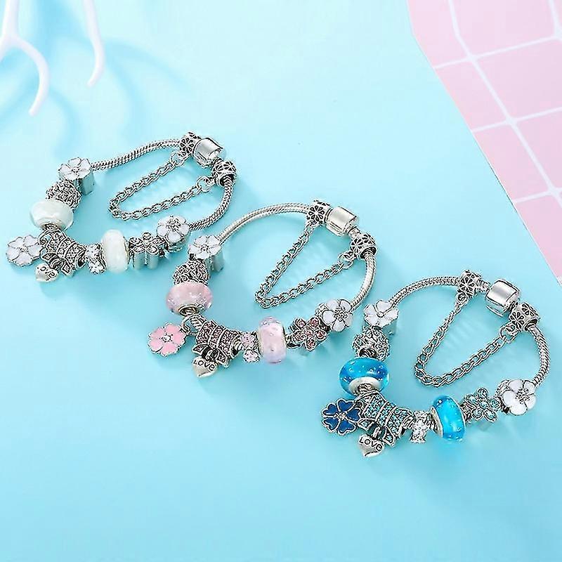 Tre sølv armbånd med charms på blå baggrund. Hvert armbånd har farverige perler og vedhæng, herunder blomster og hjerter. Perfekt til mode og smykkestil.