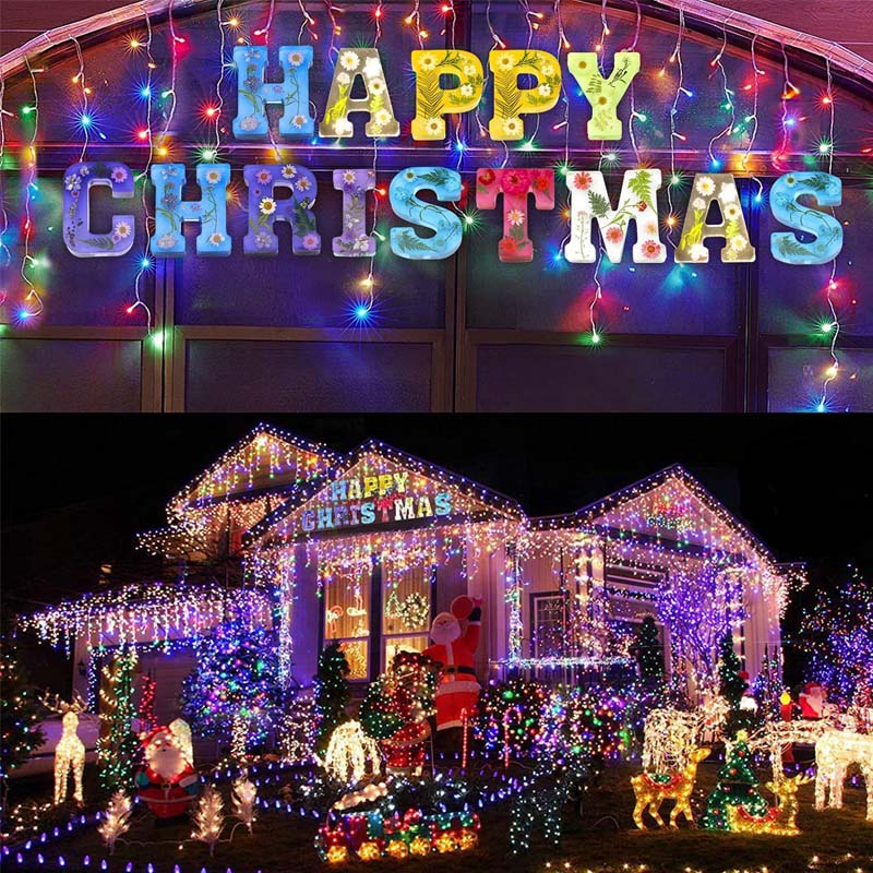 Farverig julebelysning på hus med "Happy Christmas" skilt, dekoreret med lysende rensdyr, julemand og træer. Festlig udendørs juleudsmykning.