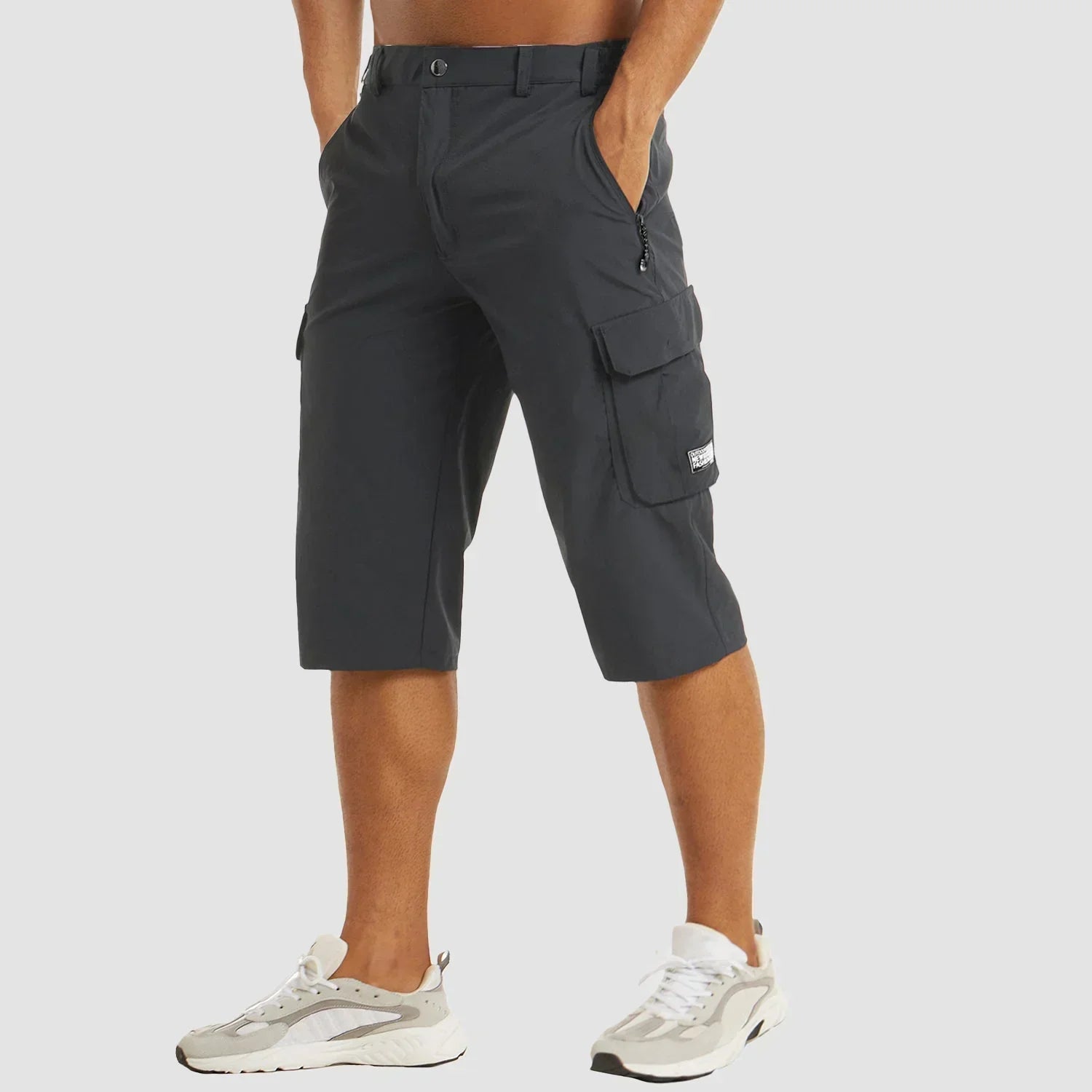 Mørkegrå cargo knickers til mænd, med sidelommer og lynlåsdetaljer, kombineret med hvide sneakers. Ideel til casual sommermode.