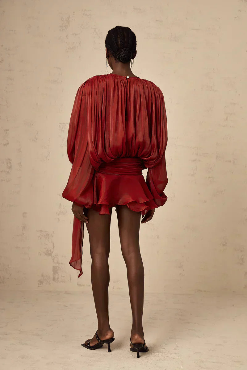 Kvinde i rød, elegant kjole med lange ærmer og flæser, set bagfra. Perfekt til festlige lejligheder. Mørk baggrund.