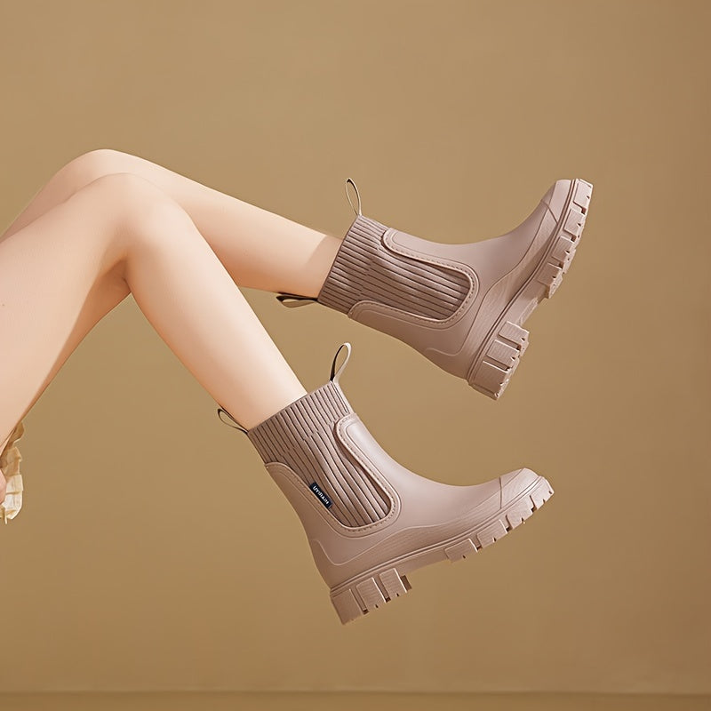 Beige ankelstøvler med chunky sål og ribstrikdetaljer, båret af en person med krydsede ben mod en neutral baggrund. Trendy fodtøj til efterår.