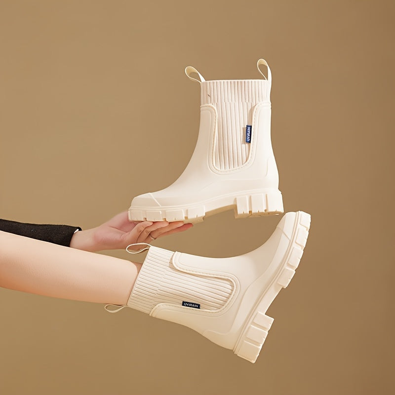Beige gummistøvler med ribbet skaft og kraftig sål, holdt af en person mod en brun baggrund. Moderne design, vandtætte støvler til kvinder.