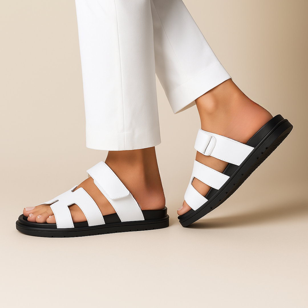 Hvide sandaler med sorte såler på kvindefødder iført hvide bukser. Komfortable, moderne fodtøj til sommermode og afslappet stil.
