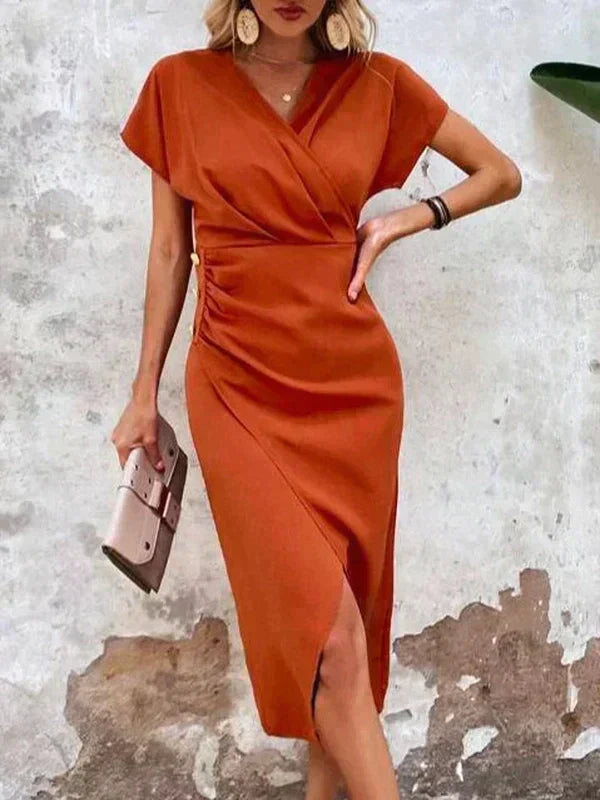 Kvinde i elegant orange kjole med slå-om design, poserer mod rustik væg. Mode, stilfuld kjole, sommeroutfit, trendy kvindetøj.