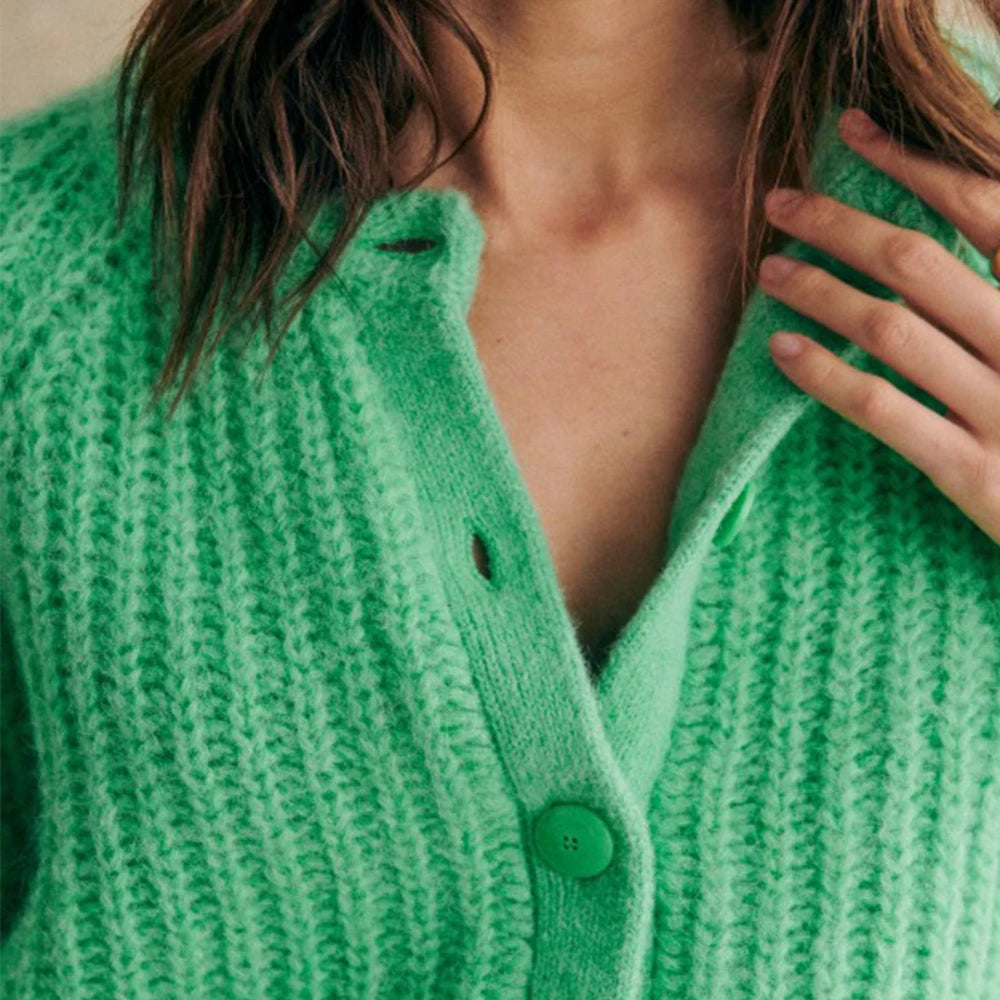 Grøn striktrøje med knapper, bæres af kvinde. Blød tekstur, moderne design. Perfekt til efterårsmode og stilfulde outfits.