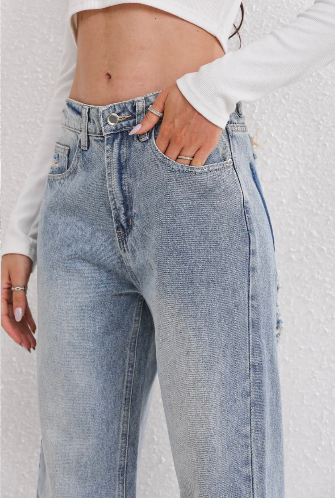 Kvinde iført lyseblå højtaljede jeans og hvid langærmet crop top. Fokus på denim mode, casual stil og trendy tøj.