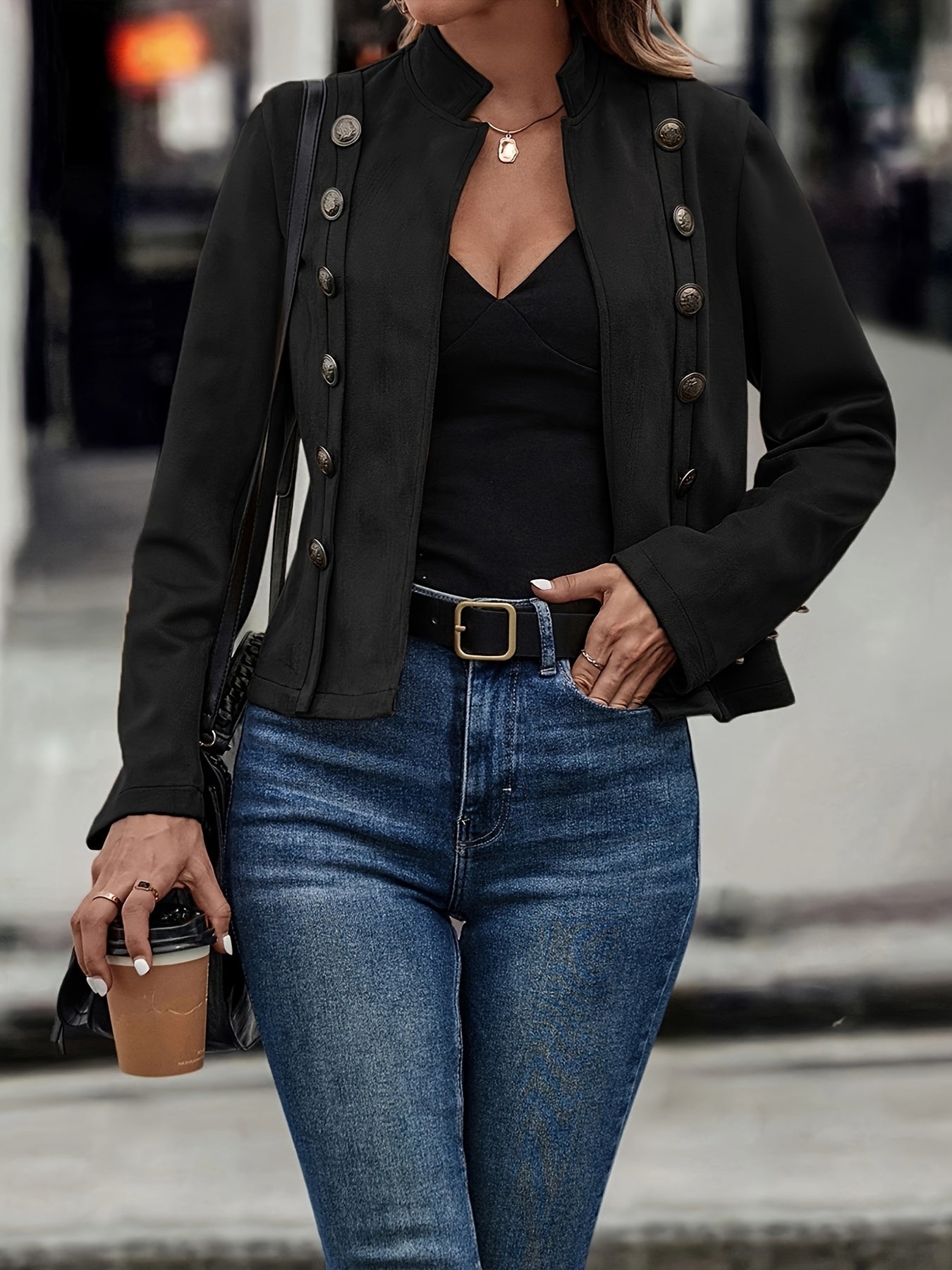 Kvinde iført sort jakke og blå jeans, holder en kaffekop. Mode, street style, casual outfit, byliv.