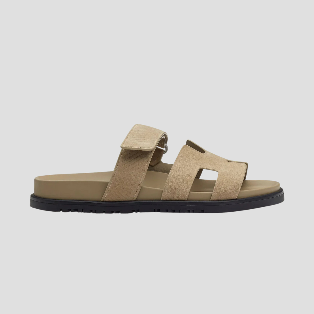 Beige lædersandal med sort sål, justerbar rem og åben tå. Komfortabel og stilfuld fodtøj til sommerbrug. Perfekt til afslappet hverdagsstil.
