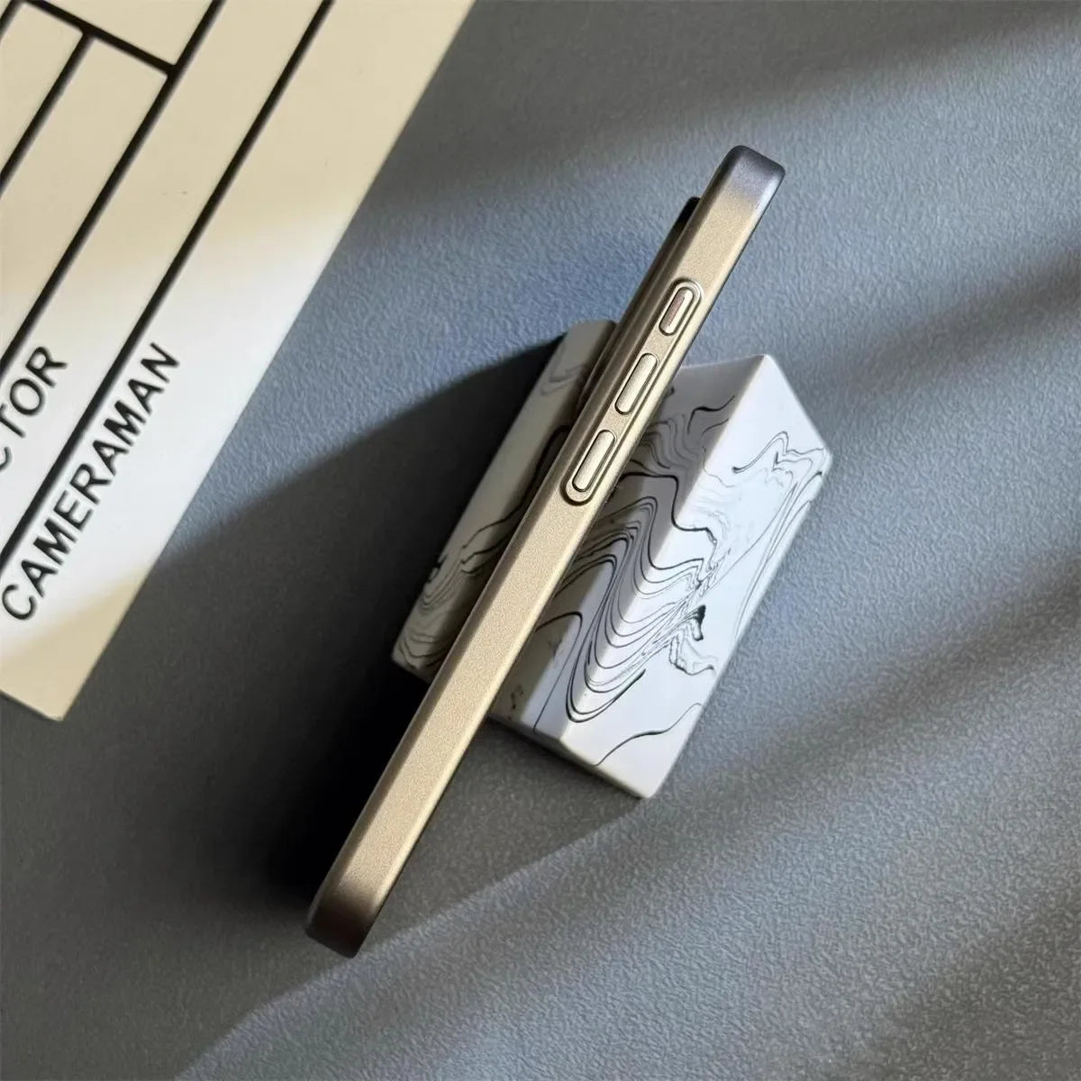 Slank smartphone i metalramme set fra siden, placeret på marmoreret holder. Moderne design, minimalistisk æstetik, teknologi, mobiltelefon.