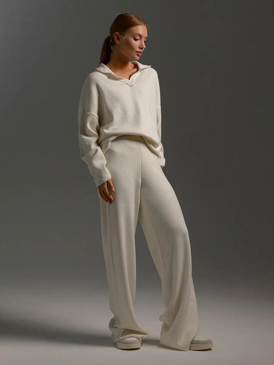 Kvinde iført hvidt, behageligt loungewear sæt med hættetrøje og brede bukser. Perfekt til afslapning og hygge. Moderne og stilfuldt design.