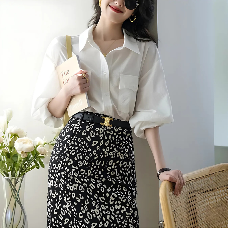 Kvinde i hvid skjorte og sort-hvid leopardmønstret nederdel, holder en bog. Moderne mode, stilfuldt outfit, trendy accessories, solbriller.