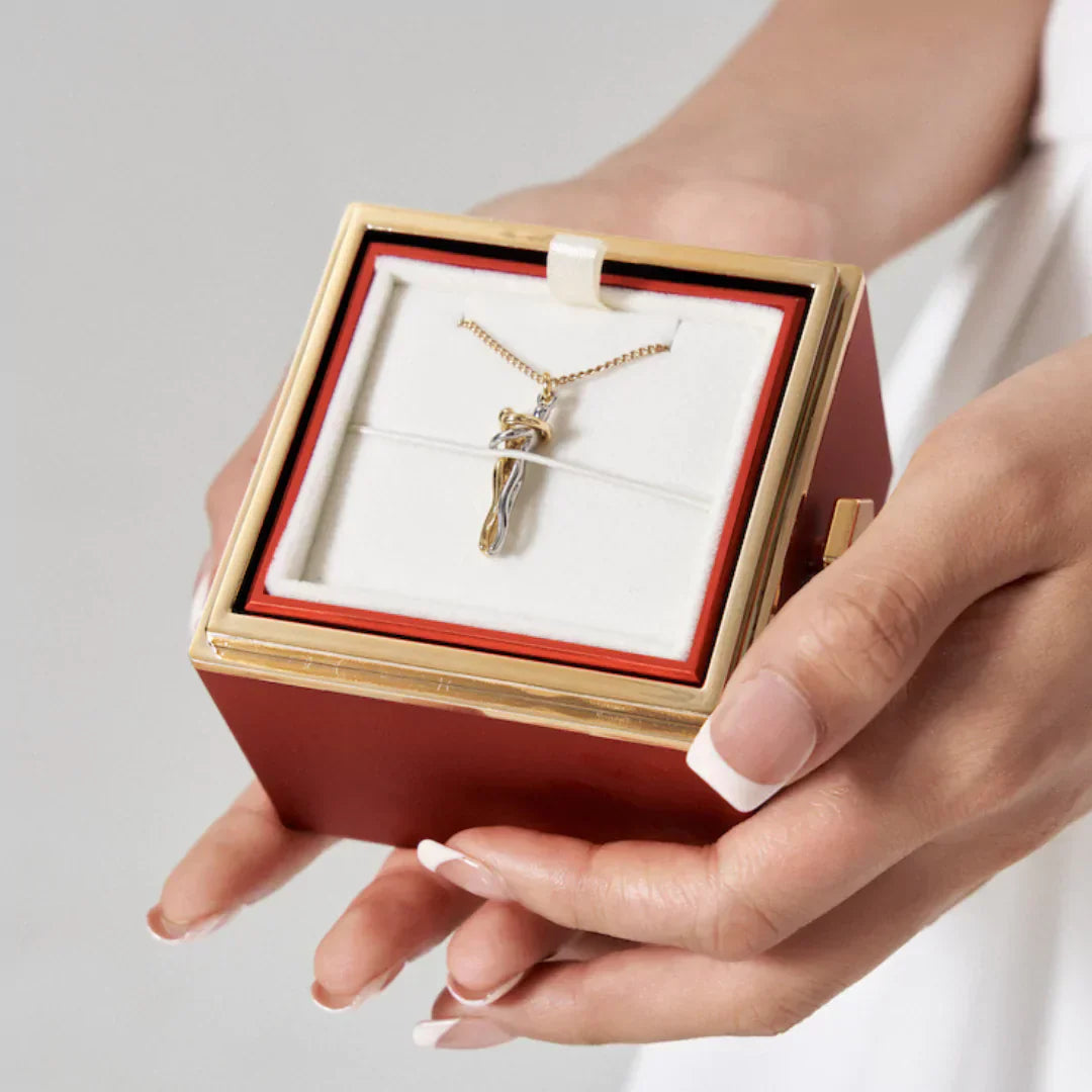 Kvinde holder rød smykkeæske med guldhalskæde og vedhæng. Elegant design, perfekt til gave. Luksus smykker, gaveidé, kvindesmykker.