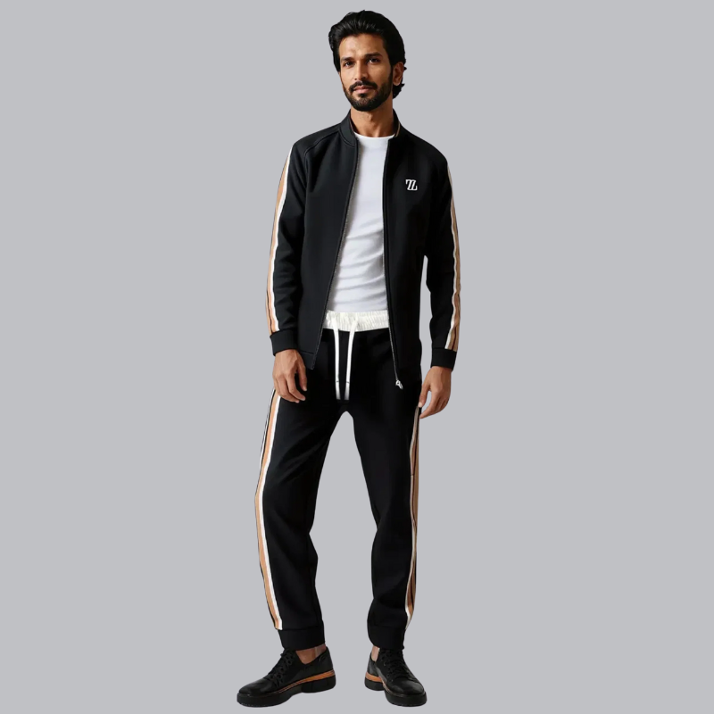 Mand iført sort træningsdragt med hvide og beige striber, hvid T-shirt og sorte sneakers. Moderne sportstøj, afslappet stil, grå baggrund.