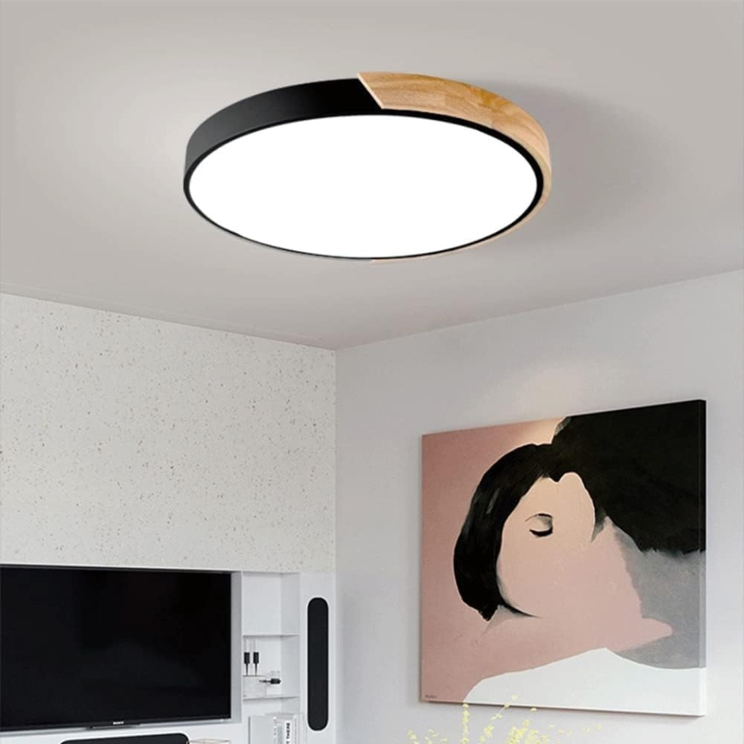 Rund moderne loftslampe i stue, minimalistisk design med sort og trædetaljer, LED-belysning, vægkunst i baggrunden.