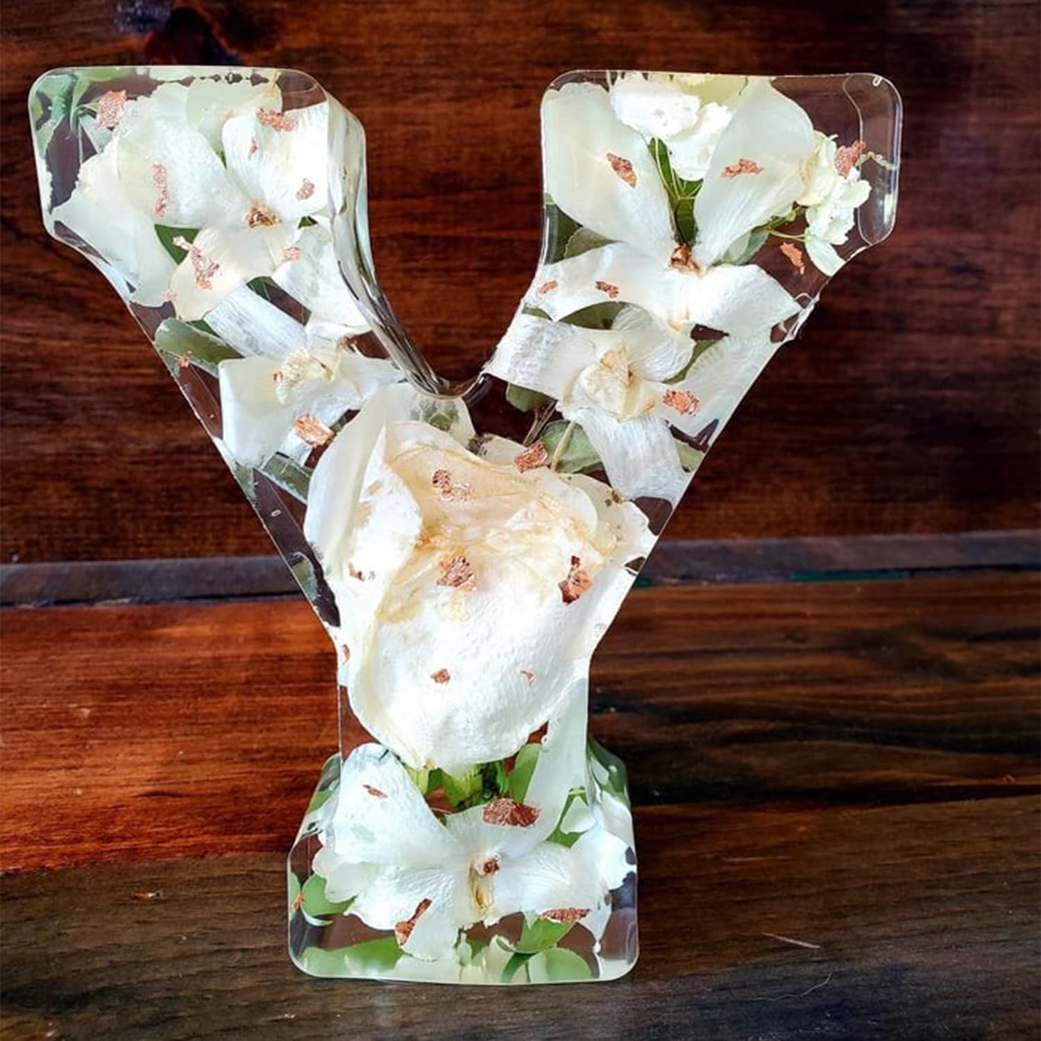 Bogstav Y i klar harpiks med indlejrede hvide blomster, placeret på en træoverflade. Unik dekoration, håndlavet kunst, naturlige elementer.