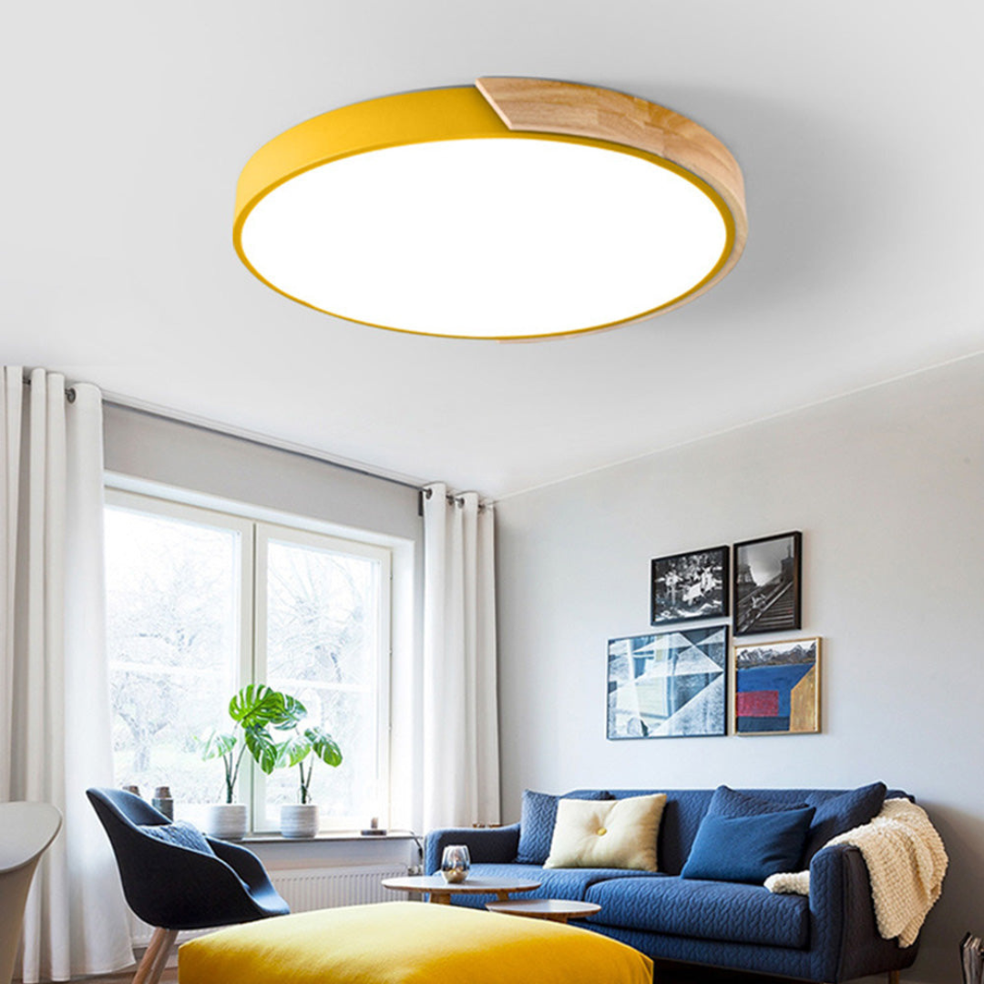 Moderne gul loftlampe i stue med blå sofa, hvide gardiner og vægkunst. LED belysning, minimalistisk design, skandinavisk indretning.