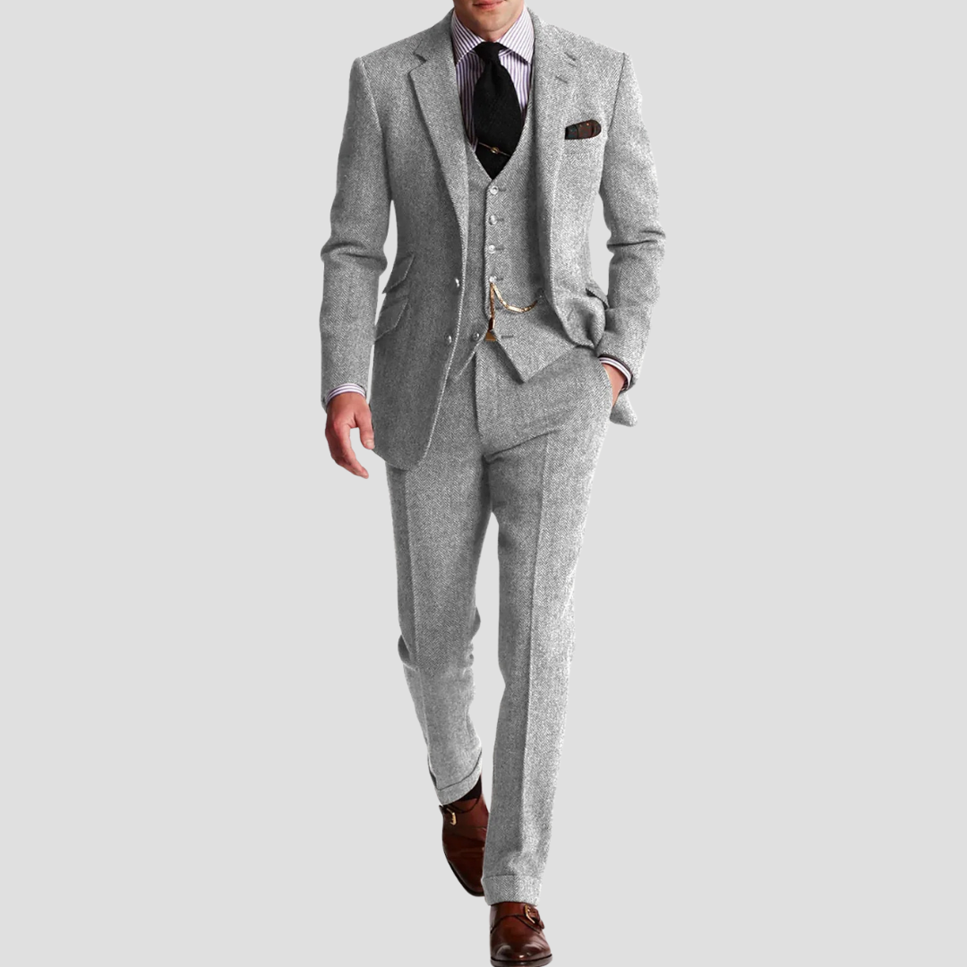 Mand iført grå jakkesæt med vest, hvid skjorte og slips, går fremad. Stilfuldt herretøj, klassisk mode, formelt outfit, brune sko.