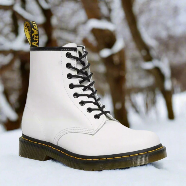 Hvid Dr. Martens støvle i sneklædt skov, klassisk design med sorte snørebånd og gul syning, vintermode, ikonisk fodtøj, udendørs stil.