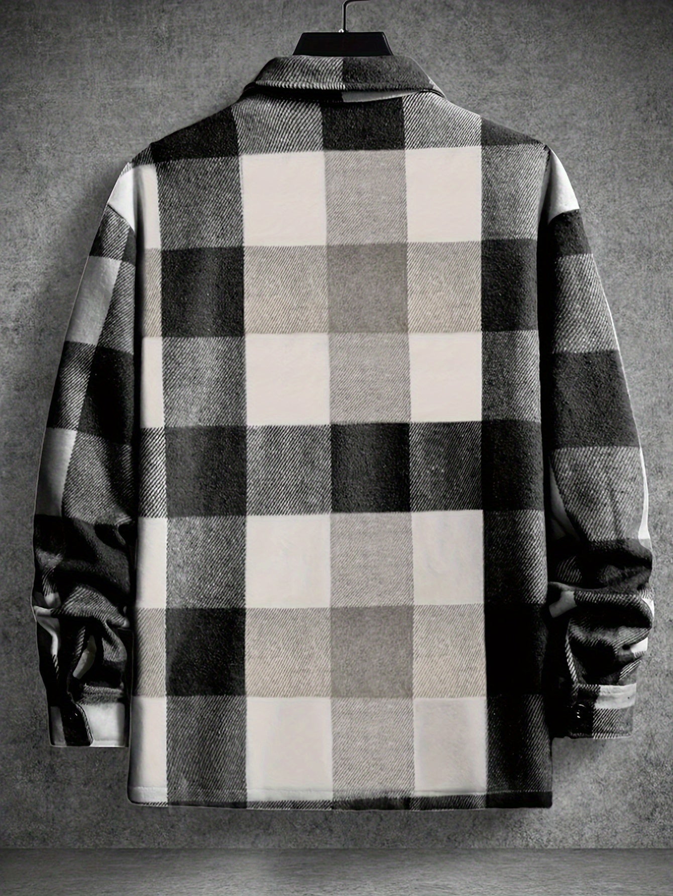 Sort-hvid ternet flanneljakke hængende på bøjle mod grå væg. Stilfuld herrejakke, klassisk design, ideel til efterår og vintermode.