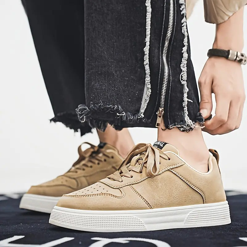 Beige sneakers med hvid sål på person iført sorte, flossede jeans. Moderne herresko, casual stil, trendy fodtøj til hverdagsbrug.