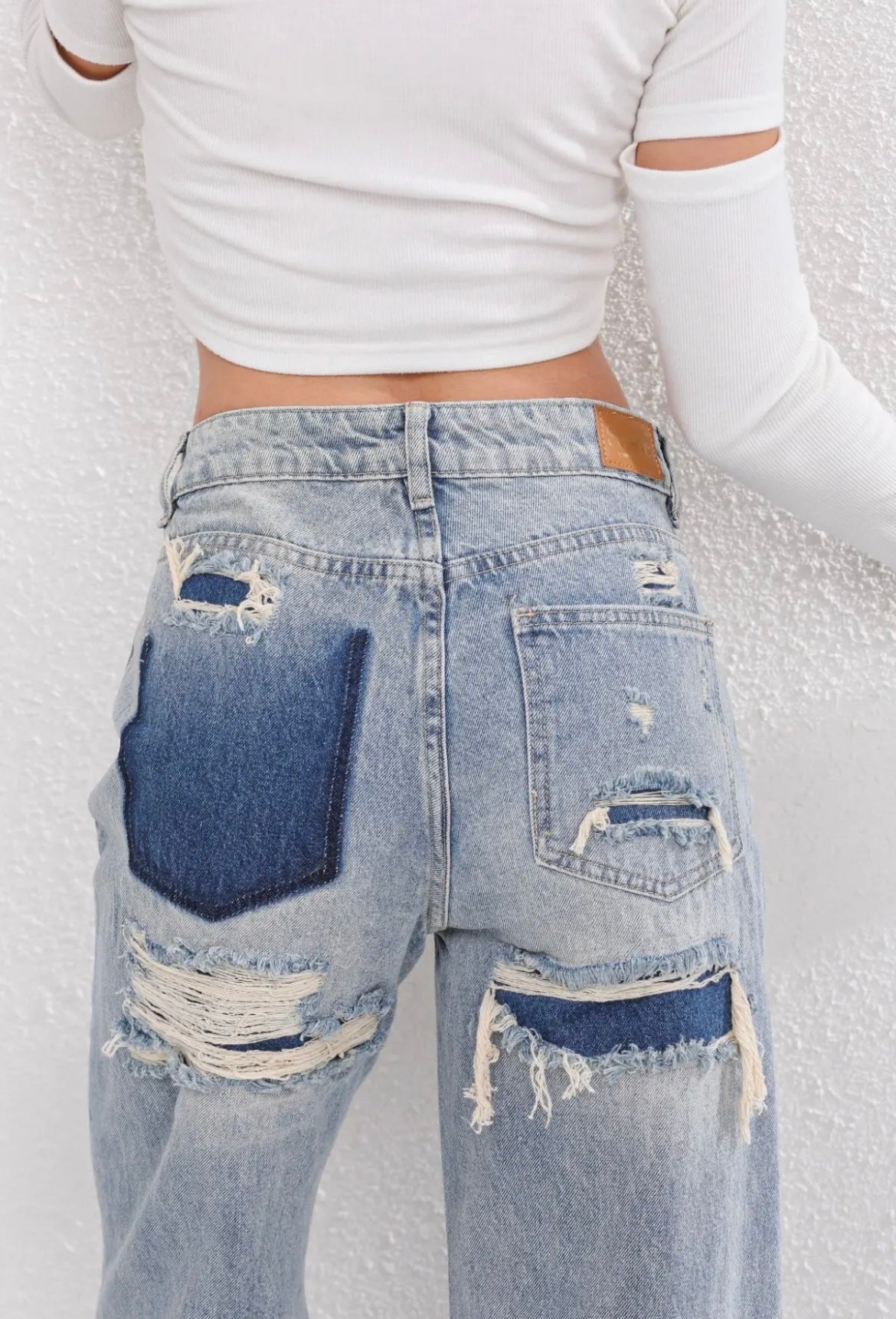 Kvinde i hvid top og slidte denimjeans med huller og lapper, set bagfra. Trendy mode, casual stil, moderne tøjdesign.