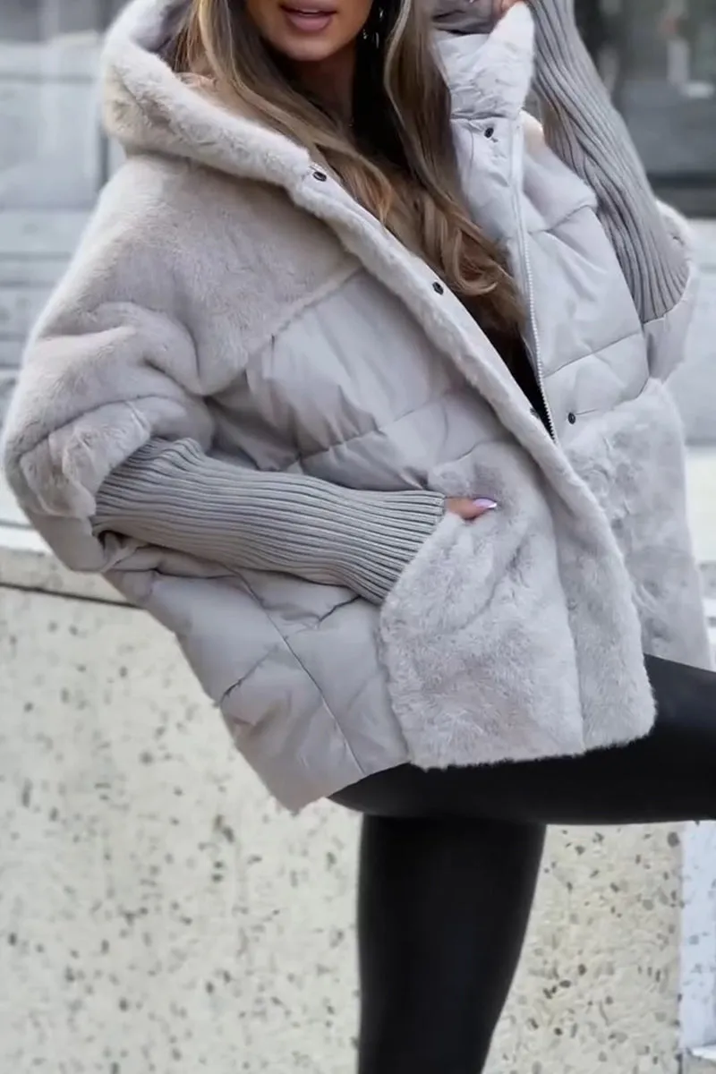 Kvinde iført stilfuld, beige pufferjakke med hætte og grå strikærmer, poserer udendørs. Vintermode, trendy overtøj, moderne look.