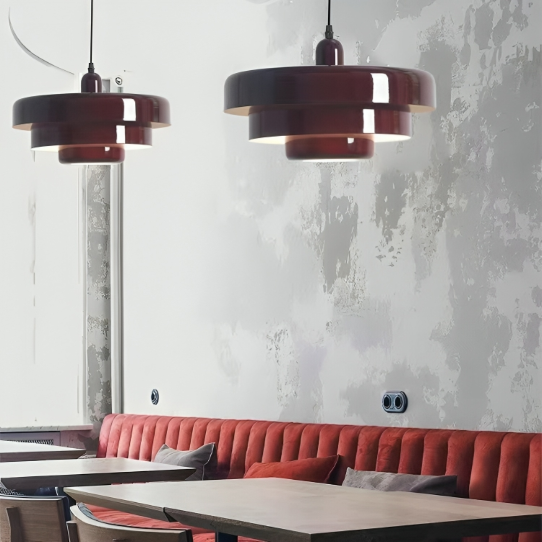 Røde pendellamper over moderne caféborde med rød polstret bænk, minimalistisk indretning, grå væg, skandinavisk design, hyggelig atmosfære.
