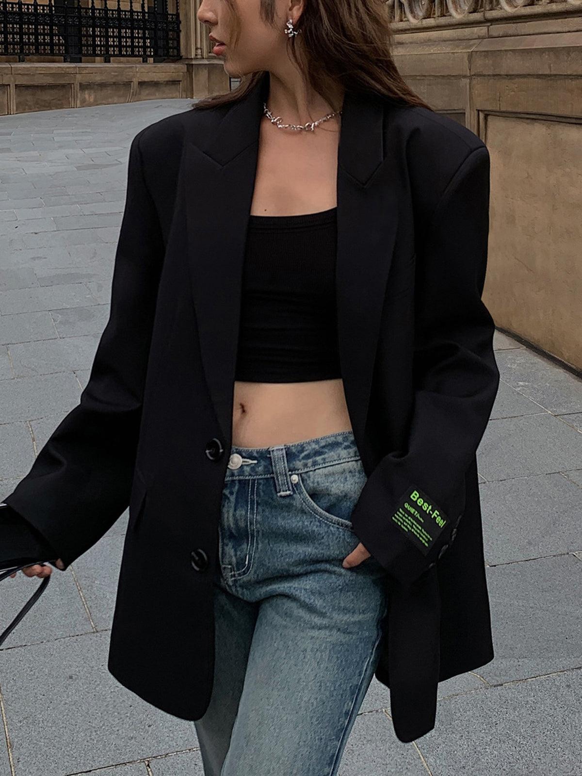 Kvinde iført sort blazer og crop top, blå jeans, står udendørs. Mode, street style, trendy outfit, casual look, moderne tøjstil.