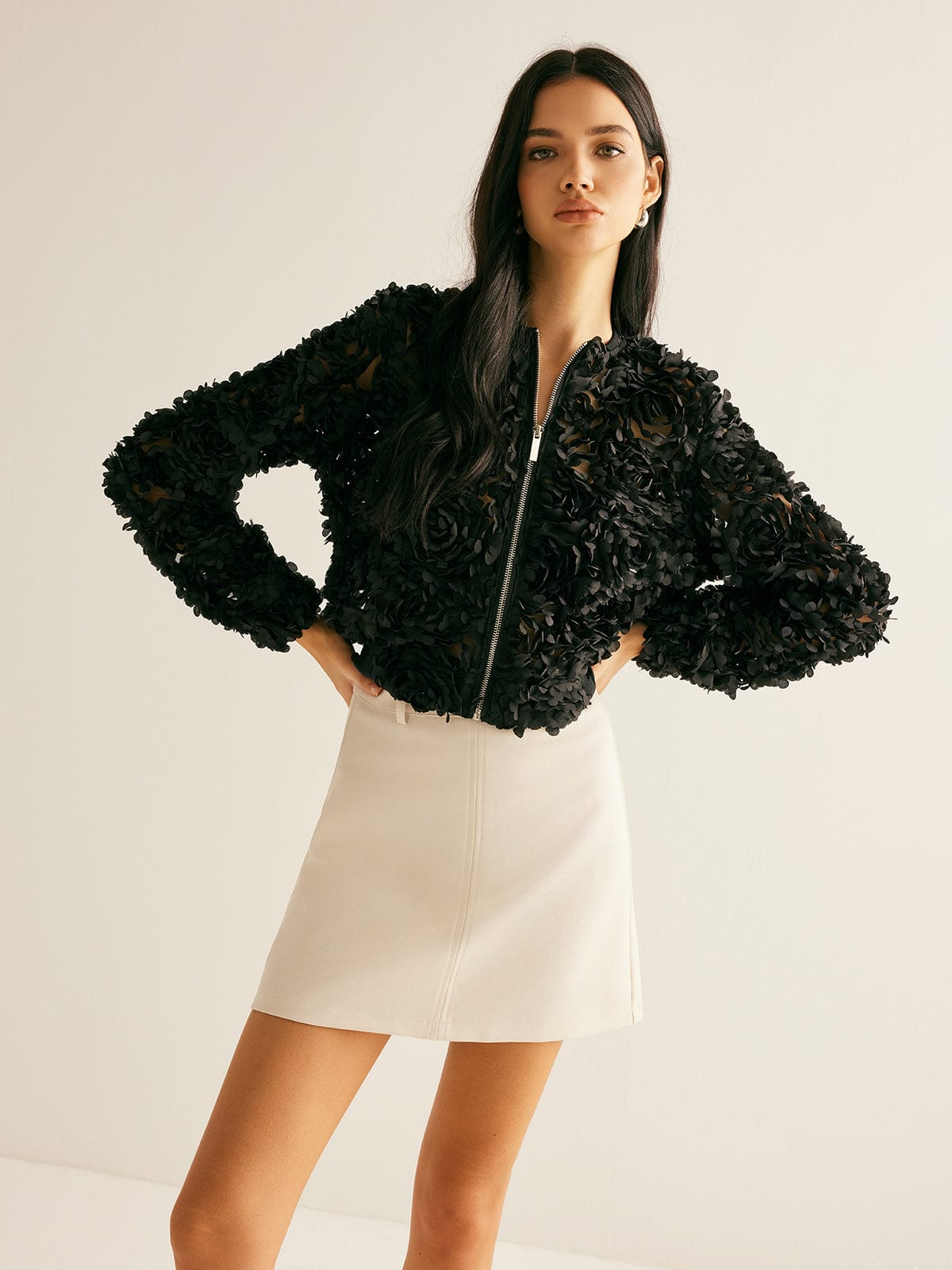 Ung kvinde iført sort blomstret jakke og hvid nederdel, poserer mod hvid baggrund. Mode, stilfuldt tøj, moderne kvindemode.