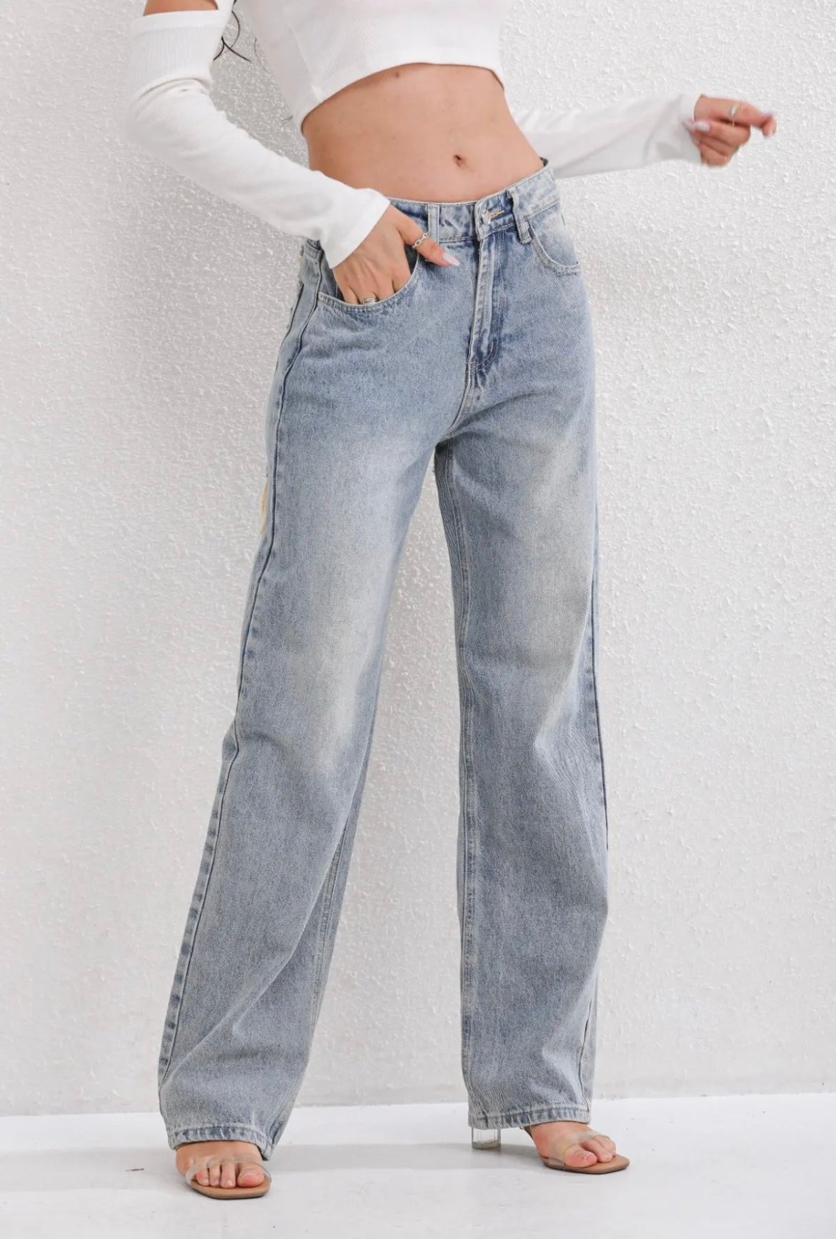 Kvinde iført lyseblå, højtaljede, løstsiddende jeans og hvid crop top. Mode, casual stil, trendy denim bukser, moderne kvindetøj.