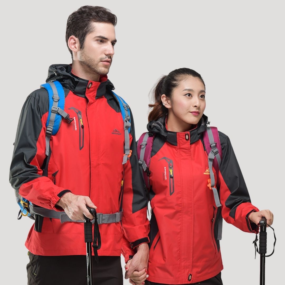 To personer iført røde vandrejakker med rygsække og vandrestave. Udendørs tøj, trekking, par, friluftsliv, eventyr, vandretur, sportstøj.