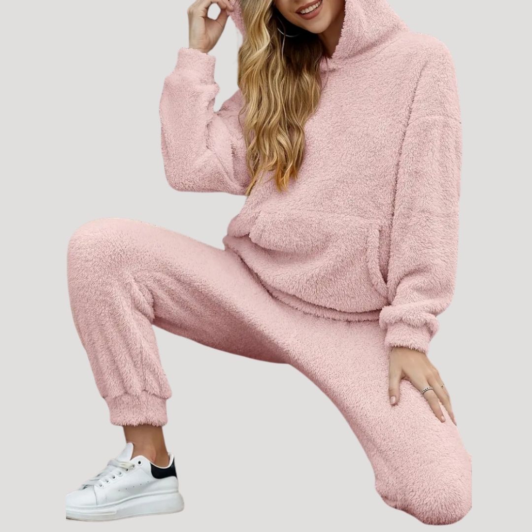 Kvinde iført lyserødt teddyfleece joggingsæt med hætte, poserer i afslappet stil. Komfortabelt loungewear, ideelt til hygge og afslapning.