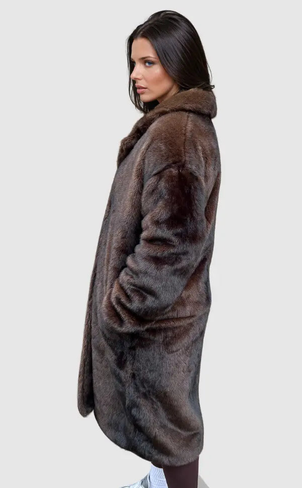 Kvinde iført brun pelsfrakke, set fra siden, med hvid baggrund. Elegant vintermode, luksuriøs pels, stilfuldt overtøj, moderne design.