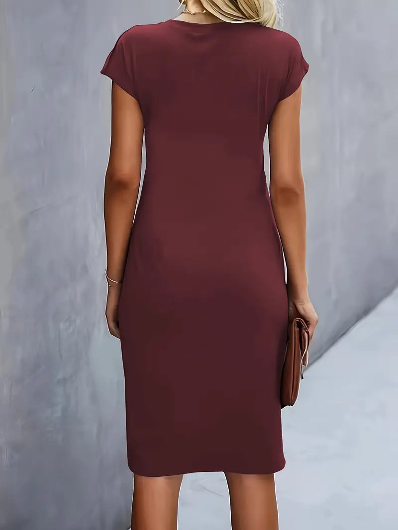 Kvinde i enkle, tætsiddende bordeaux kjole set bagfra, står mod grå væg, holder brun clutch. Elegant, minimalistisk mode, sommerkjole.