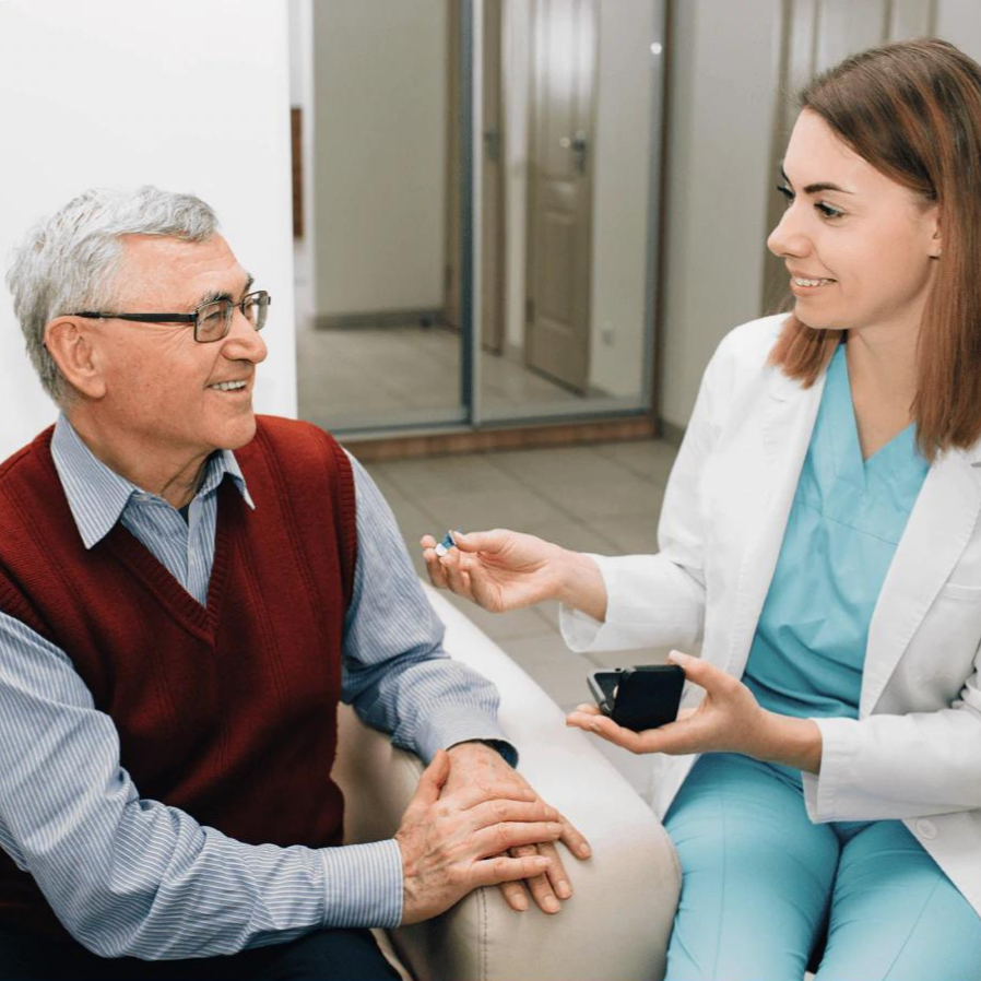 Ældre mand taler med kvindelig læge i hvid kittel, der holder en medicinsk enhed. Sundhedskonsultation, læge-patient interaktion, medicinsk rådgivning.