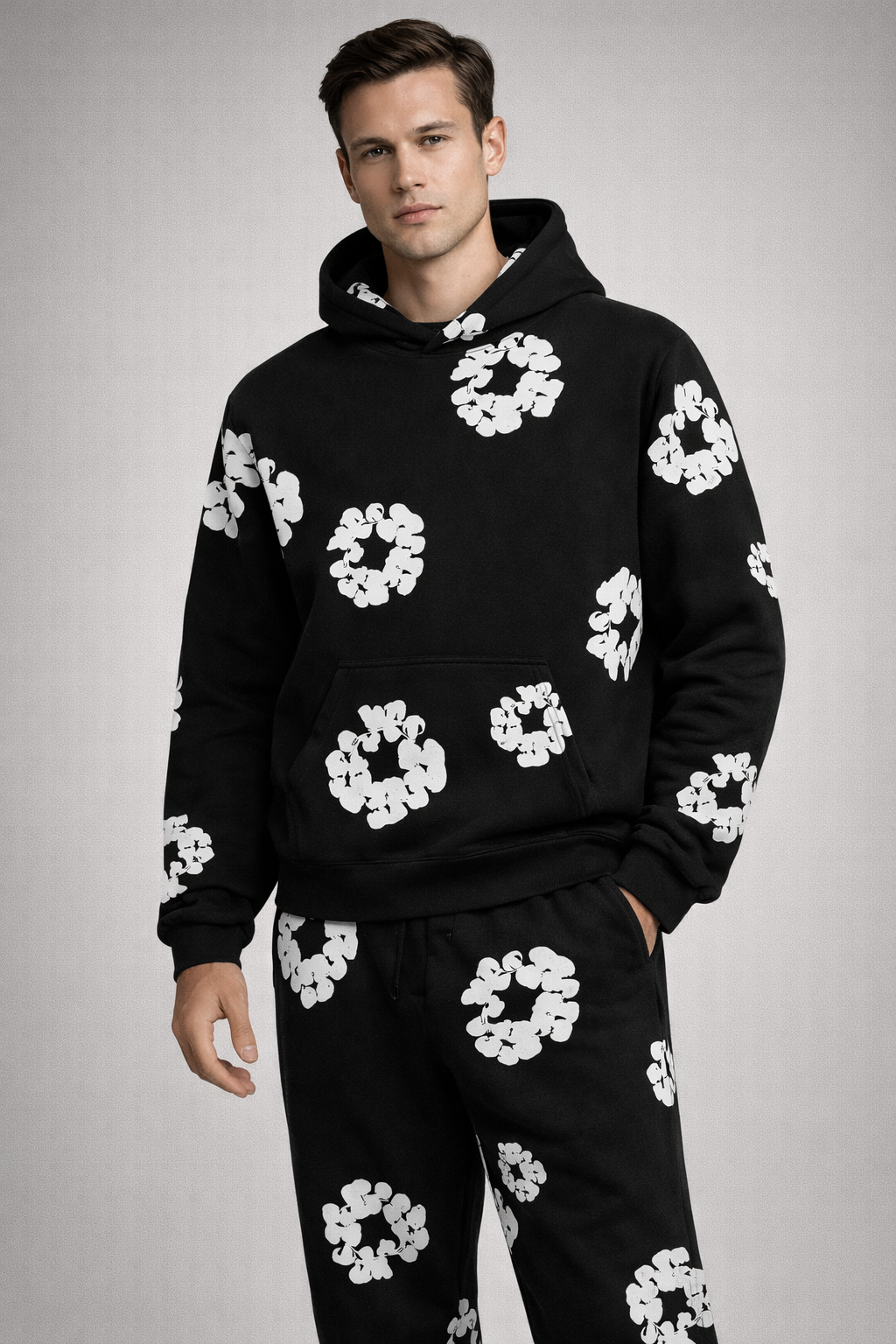 Mand iført sort hættetrøje og bukser med hvidt blomstermønster. Moderne streetwear, afslappet stil, trendy herremode, komfortabelt tøj.