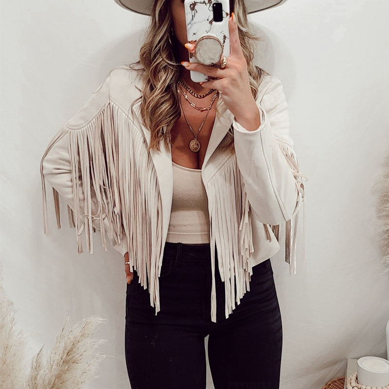 Kvinde i hvid frynsejakke, sort bukser og hat tager selfie. Moderne boho-stil, trendy mode, casual outfit.