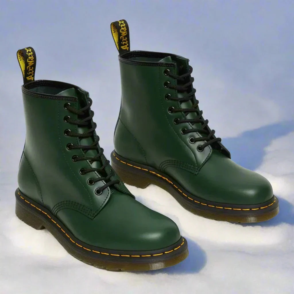 Grønne Dr. Martens støvler i sne, klassisk design med sorte snørebånd og gul syning. Populære vinterstøvler, robust og stilfuldt fodtøj.