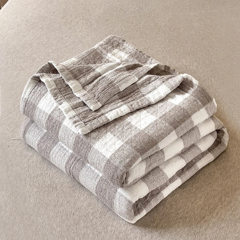Grå og hvid ternet plaid tæppe på beige baggrund, blødt og hyggeligt design, perfekt til stueindretning og komfort.