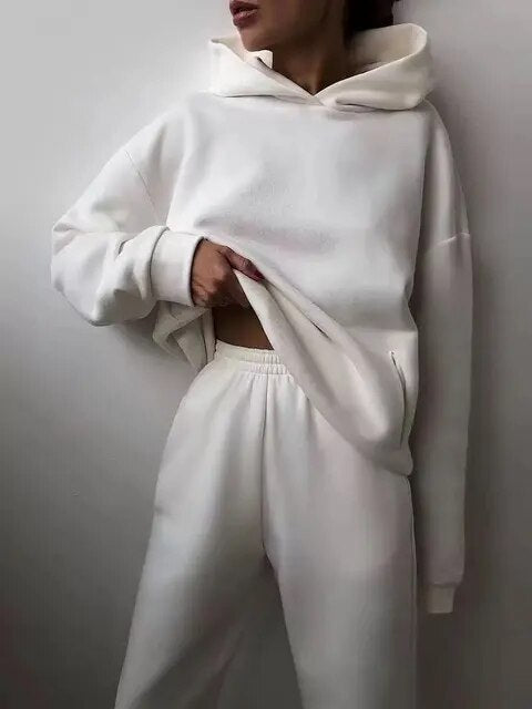 Person iført hvid hættetrøje og joggingbukser, afslappet tøjstil, minimalistisk mode, komfortabelt loungewear, moderne streetwear look.