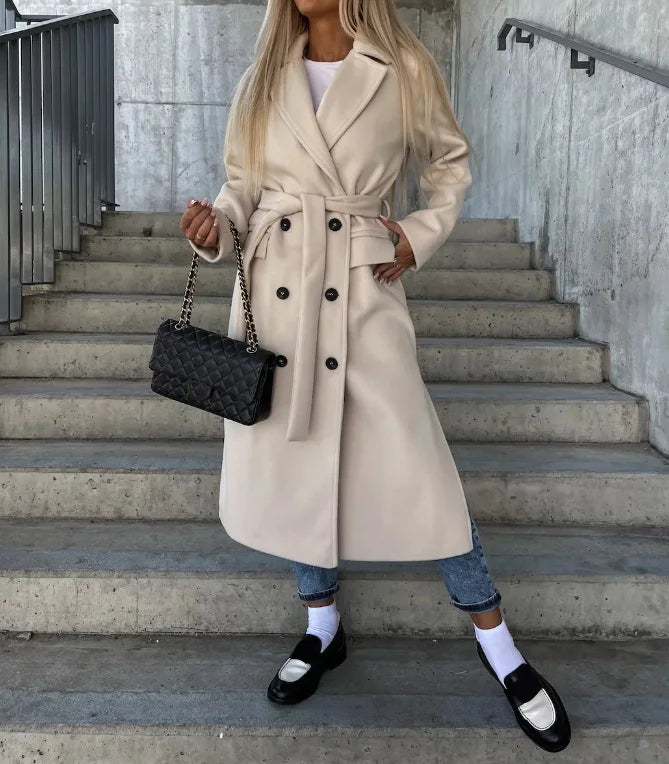 Kvinde i beige trenchcoat på trappe, bærer sort quiltet taske. Mode, efterårstøj, stilfuldt look, klassisk frakke, trendy accessories.