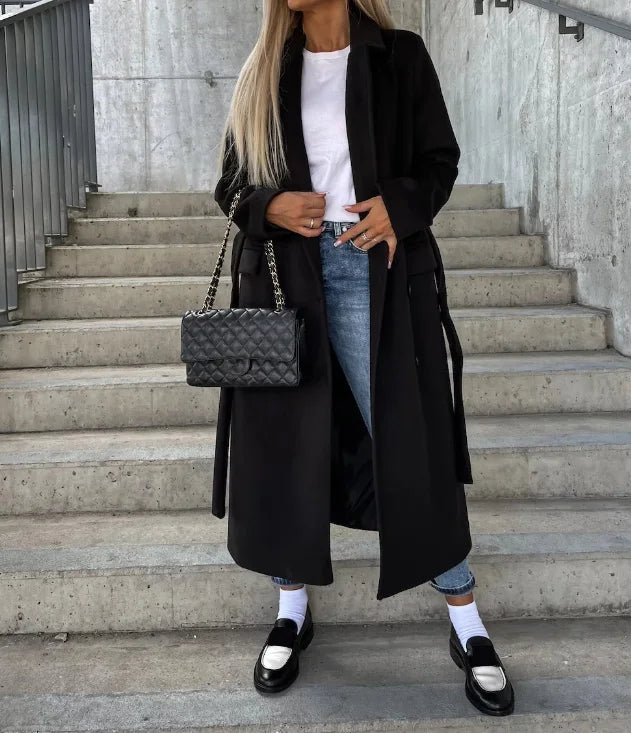 Kvinde i sort frakke og jeans på trappe, bærer en quiltet håndtaske. Mode, street style, elegant outfit, moderne kvindetøj, trendy accessories.