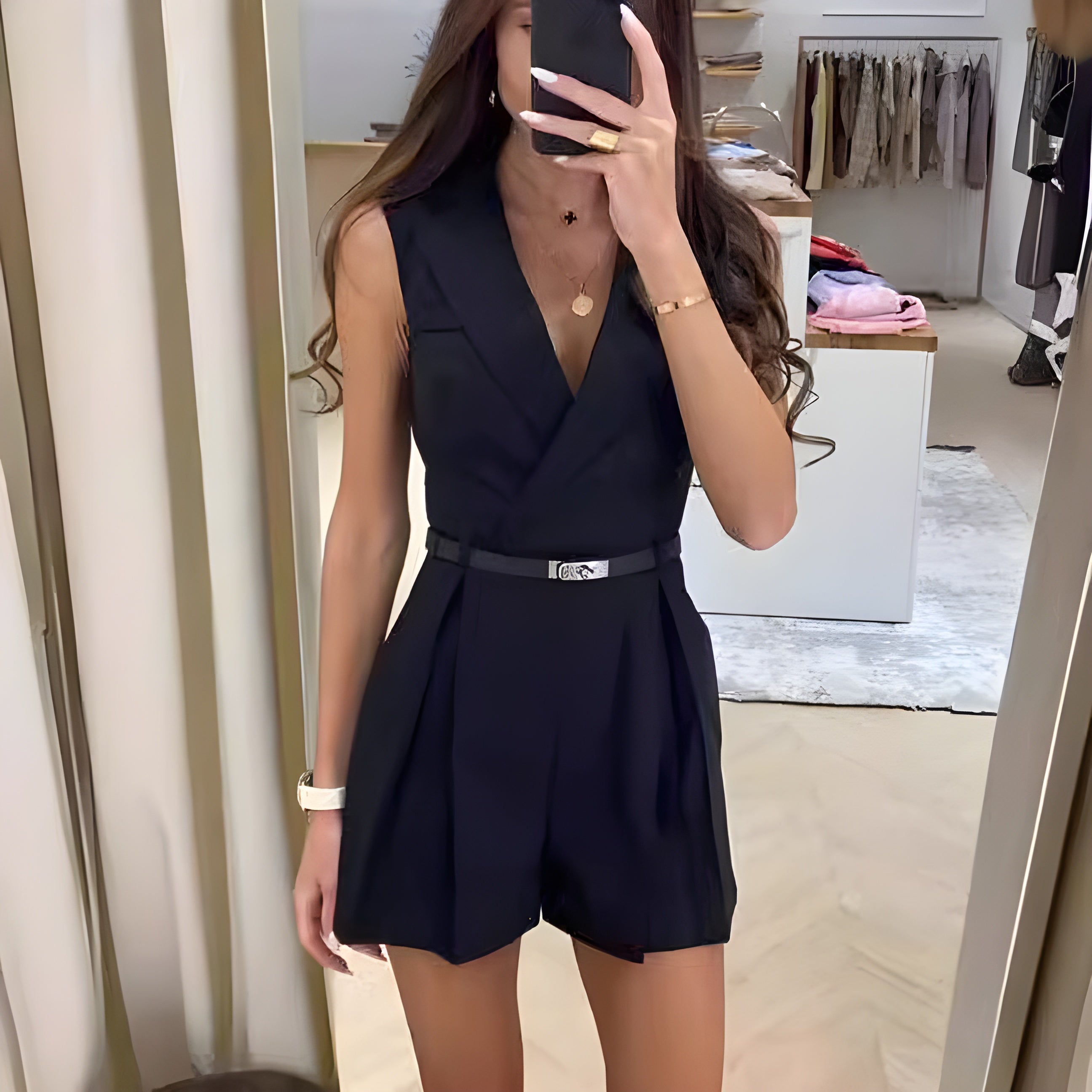 Kvinde i sort jumpsuit tager selfie i moderne tøjbutik. Stilfuldt outfit, mode, shopping, spejl, elegant design, trendy beklædning.