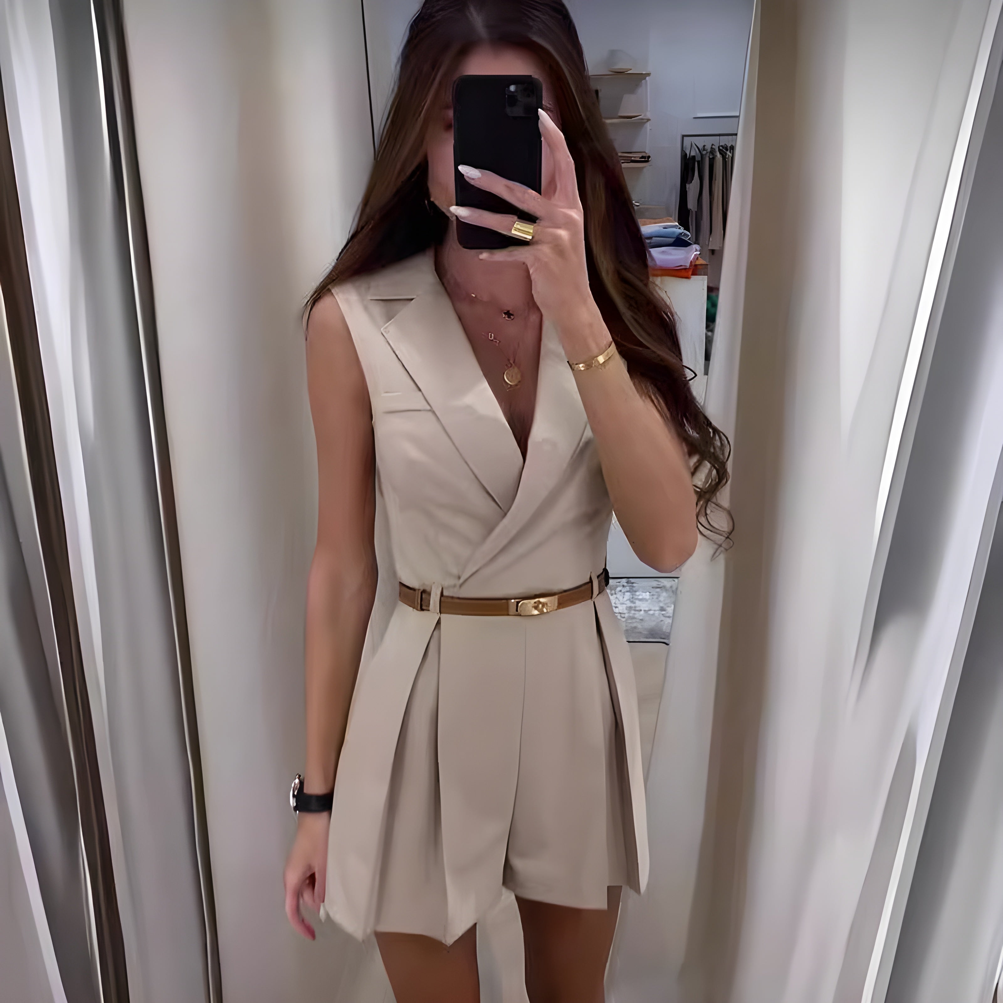 Kvinde i beige jumpsuit med bælte, spejlbillede, langt hår, guldtilbehør. Moderne mode, elegant stil, trendy outfit, selfie i garderobe.